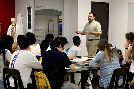 Estudiantes del Rivermont Collegiate están sentados en el aula escuchando a un profesor masculino.