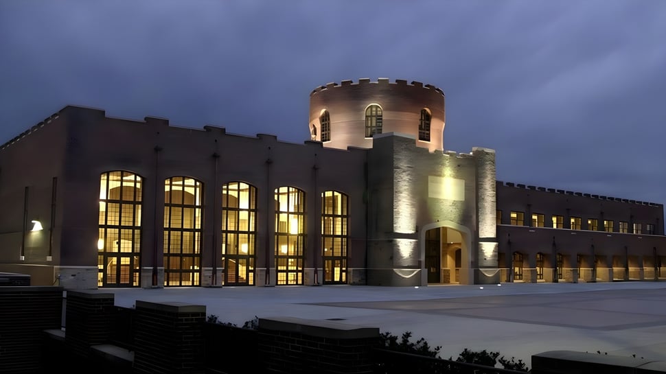El edificio de Riverside Military Academy recuerda a un castillo con ventanas iluminadas y una alta torre bajo un cielo nublado.