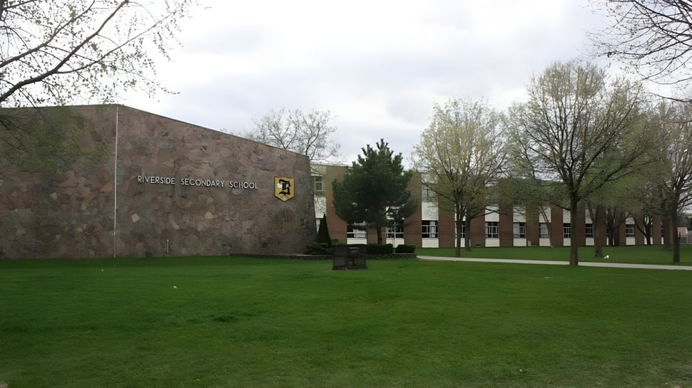 Un patio cubierto de hierba frente a un edificio de ladrillo con ventanas de arco en el terreno de la Riverside Secondary School.