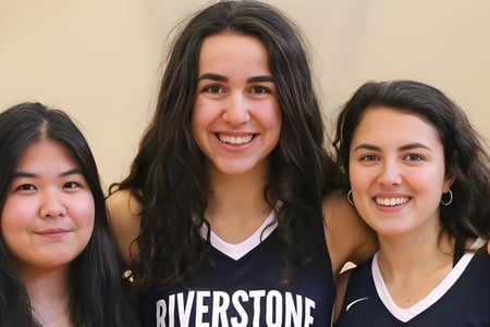 Tres alumnas con cabello oscuro sonríen y posan juntas en un ambiente relajado en el campus de la Riverstone International School.