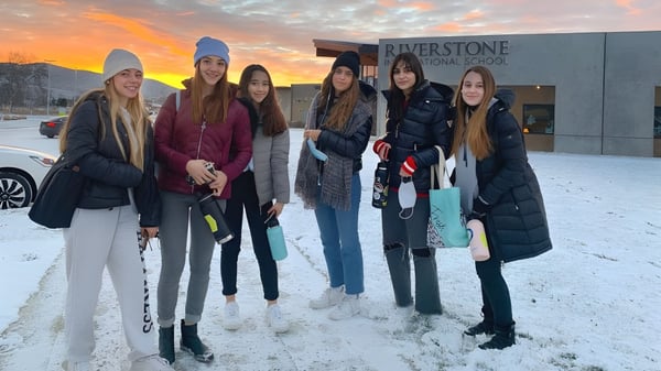 Un grupo de alumnas está en el exterior nevado del campus de la Riverstone International School al atardecer.