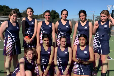 Un grupo de jóvenes atletas posan en el campo deportivo de la Riverton and District High School frente a árboles y edificios.