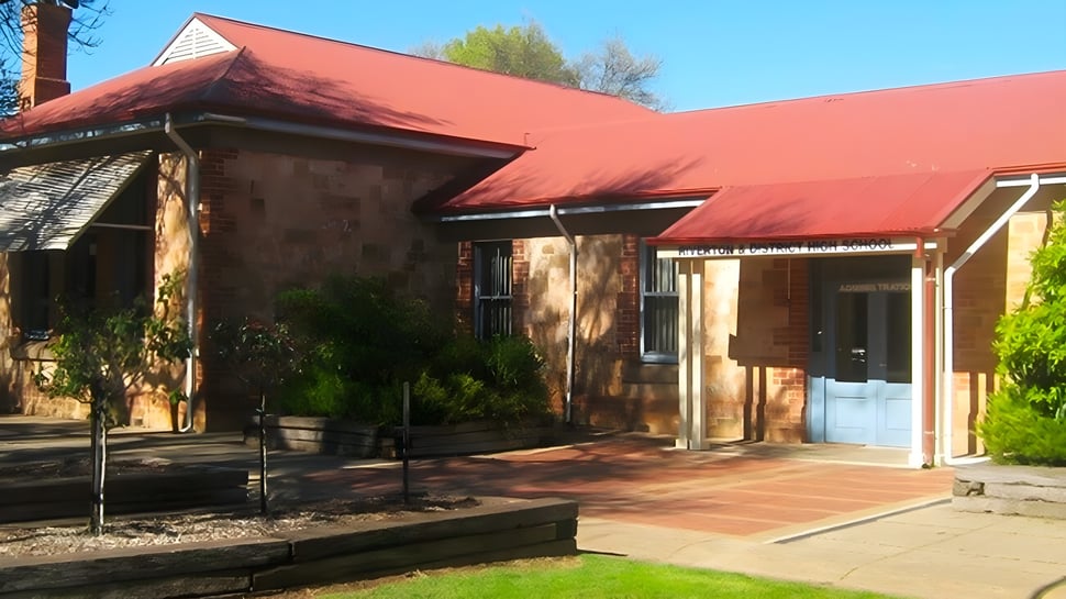 El edificio similar al adobe con techo de tejas rojas se encuentra en el campus de la Riverton and District High School en un entorno verde.