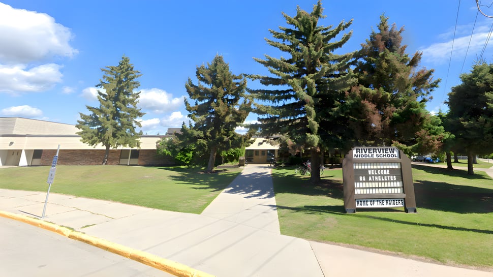Una pradera con altos árboles de hoja perenne frente a un edificio en el terreno de la Riverview Middle School.