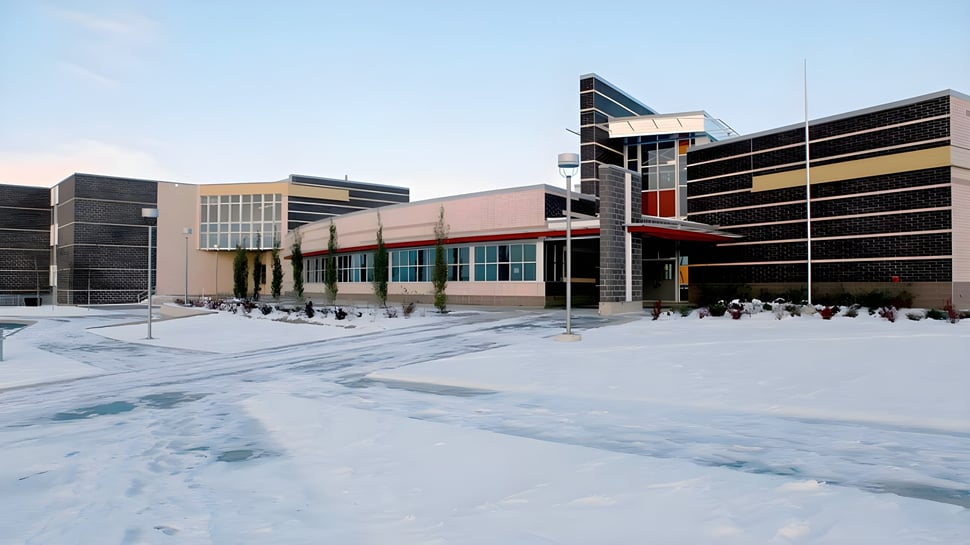 El moderno edificio de varios pisos con fachada de vidrio de la Robert Thirsk High School está rodeado de un paisaje nevado.