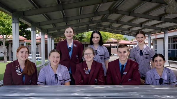 Un grupo de estudiantes de la Robina State High School está en uniformes rojos uniformes bajo una estructura exterior cubierta.