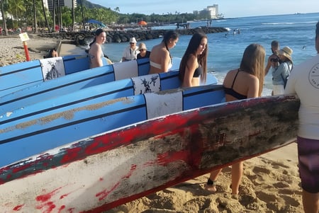 Un grupo de estudiantes de la Robina State High School está en la playa junto a coloridas tablas de surf con vista a la ciudad de fondo.