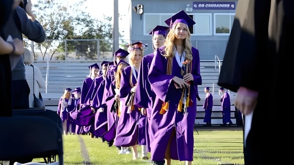 Estudiantes de la Rockford Lutheran School con togas de graduación moradas caminan en un campo de hierba frente a un edificio escolar.