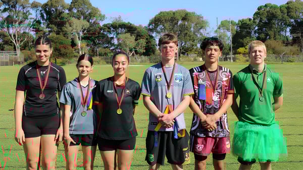 Un grupo de jóvenes atletas de la Rockingham Senior High School está en un campo de hierba bajo un cielo azul.
