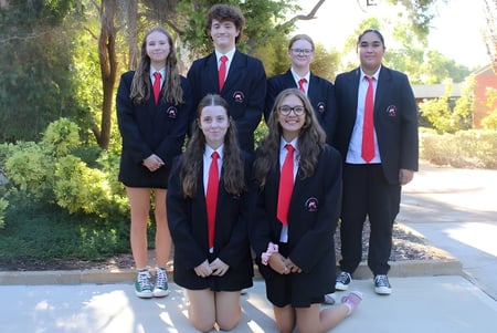 Un grupo de seis estudiantes de la Rockingham Senior High School está vestido formalmente en el área exterior verde de la escuela.