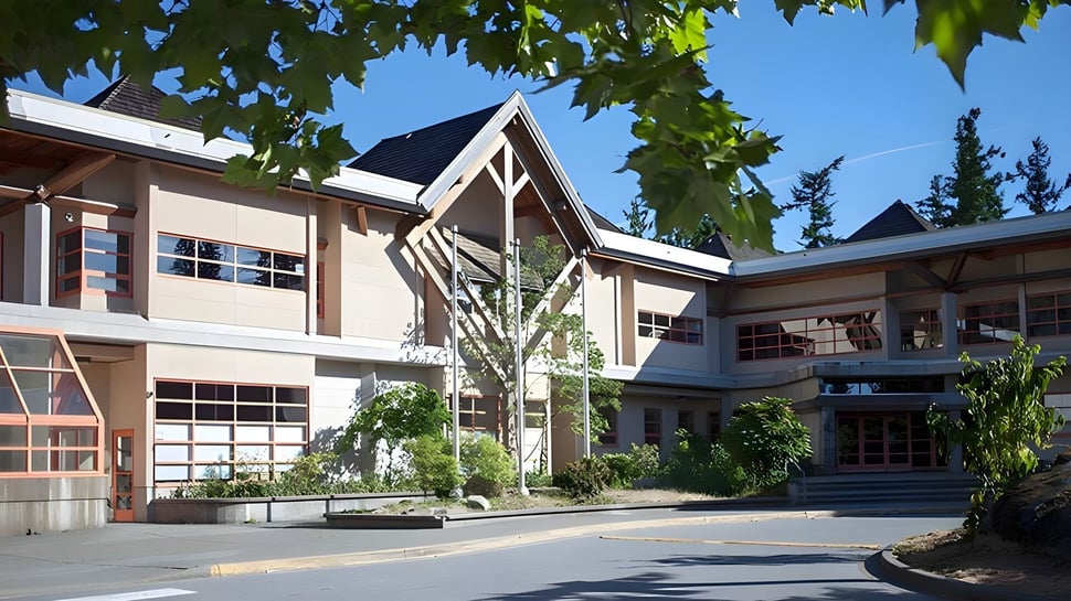 El moderno edificio de varios pisos de la Rockridge Secondary School está rodeado de exuberante vegetación y cielo azul.