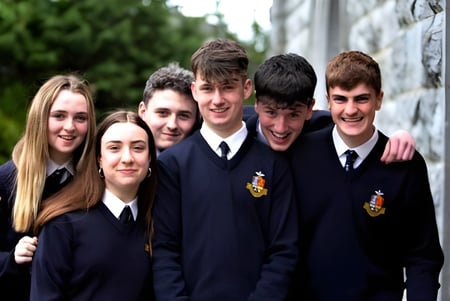 Un grupo de estudiantes del Rockwell College está junto a una pared de piedra con plantas verdes.