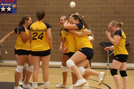 Un grupo de jóvenes jugadoras de voleibol de la Rockwell Charter School celebra en la cancha de baloncesto.