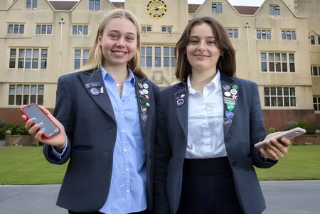 Dos alumnas de la Roedean School están de pie con ropa formal frente a un edificio histórico con torre del reloj en el campus escolar.