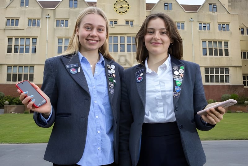 Dos alumnas de la Roedean School están de pie con ropa formal frente a un edificio histórico con torre del reloj en el campus escolar.
