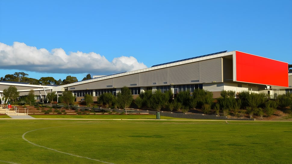 El moderno edificio principal del Roma Mitchell Secondary College se encuentra frente a un prado con árboles bajo un cielo azul.