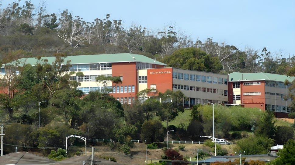 El edificio escolar de varios pisos de la Rose Bay High School con fachadas coloridas está rodeado de árboles verdes.