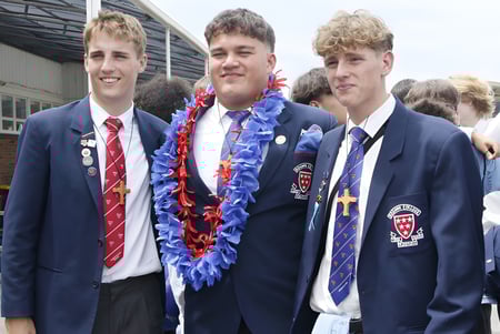Tres alumnos en uniforme escolar están juntos con guirnaldas de flores en el campus del Rosmini College.