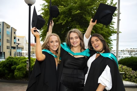 Tres alumnas de Rosny College celebran su graduación frente a un horizonte urbano.