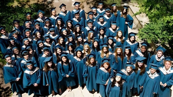 Un gran grupo de graduados de la Ross School está de pie con togas y birretes azules al aire libre frente a árboles y áreas verdes.