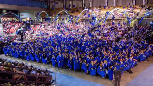 Graduadas y graduados de la Ross Sheppard High School llevan togas azules durante su ceremonia de graduación en un auditorio lleno.