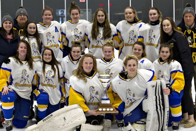 Un grupo de jóvenes jugadoras de hockey del Rosseau Lake College posan junto a un trofeo en una pista de hielo.