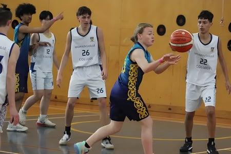 Estudiantes de la Rotorua Lakes High School juegan baloncesto en el gimnasio con paredes de madera y decoraciones al fondo.