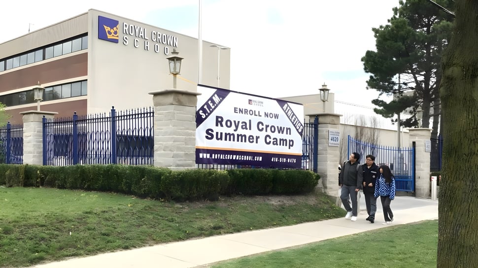 El edificio de la Royal Crown School con el cartel Royal Crown Summer Camp y personas en la acera delante.