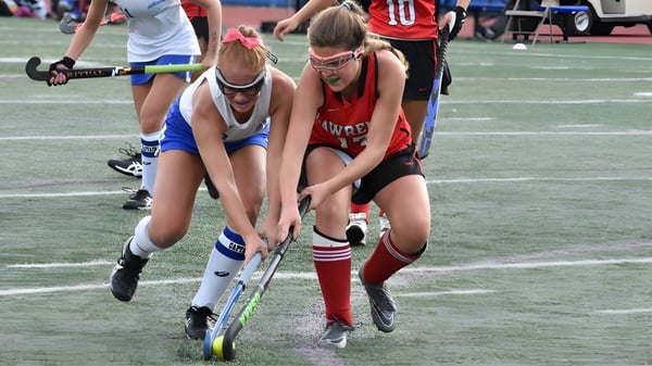 Dos estudiantes de la Royal High School juegan un partido de hockey sobre campo y luchan por la posesión del balón.