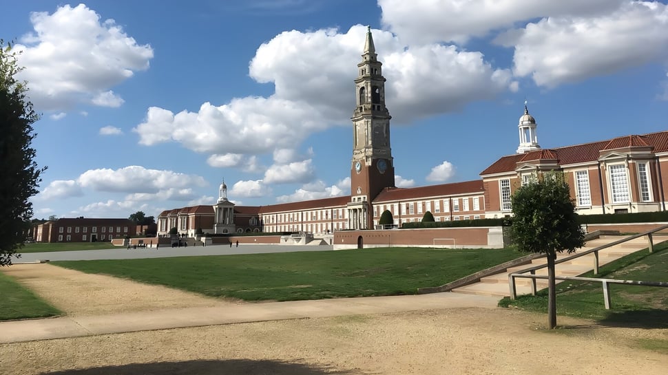 El gran edificio con una alta torre se encuentra en el terreno de la Royal Hospital School frente a una superficie de césped con un camino de grava.