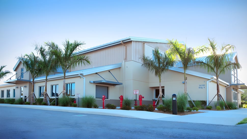 El moderno edificio de dos pisos con techo azul de la Royal Palm Academy está rodeado de palmeras bajo un cielo despejado.