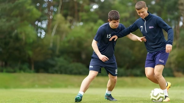 Dos estudiantes de la Royal Russell School están jugando al fútbol en un campo de hierba rodeado de árboles.
