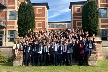 Un gran grupo de estudiantes está posando para una foto grupal frente a un edificio de ladrillo de la Royal Russell School con paredes cubiertas de hiedra.
