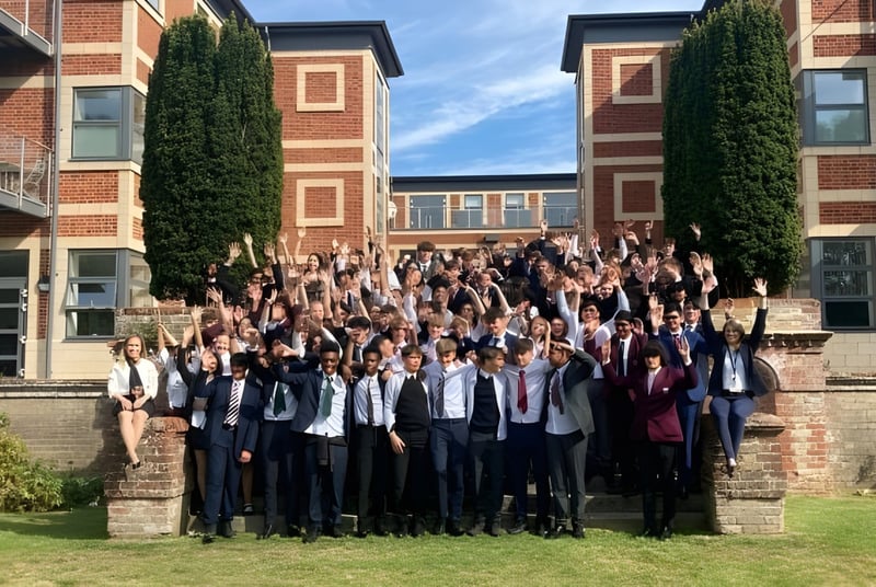 Un gran grupo de estudiantes está posando para una foto grupal frente a un edificio de ladrillo de la Royal Russell School con paredes cubiertas de hiedra.
