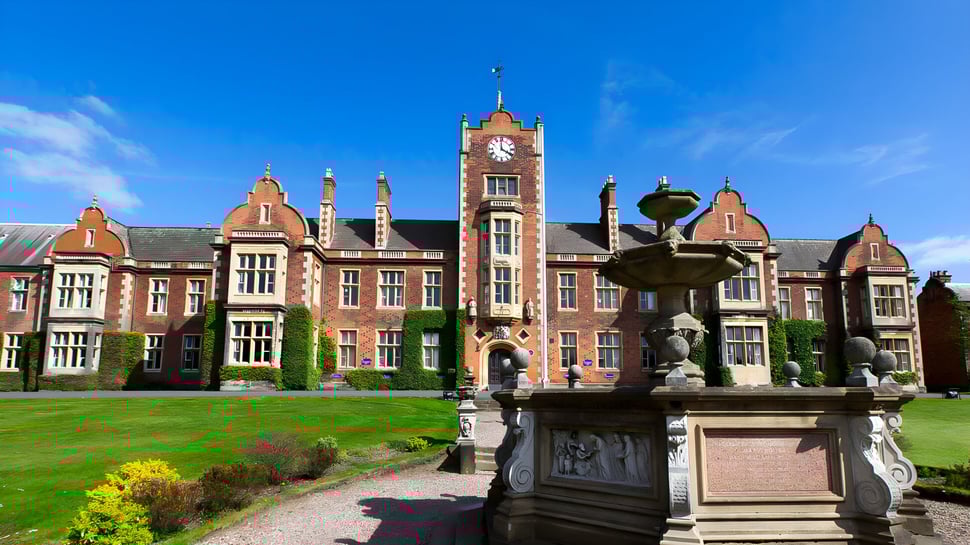 El histórico edificio principal con torre del reloj de The Royal School Wolverhampton se encuentra en un jardín cuidado con fuente.