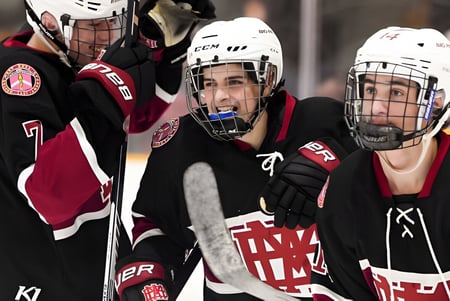 Tres jugadores de hockey sobre hielo en uniforme en el hielo, uno lleva una camiseta con las letras A y M, en el campo de hielo de la Royal Vale High School.
