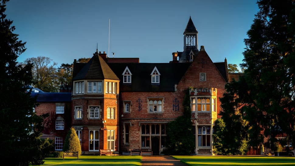 El edificio histórico de ladrillo de la Rugby School con una alta torre está rodeado de hojas verdes.