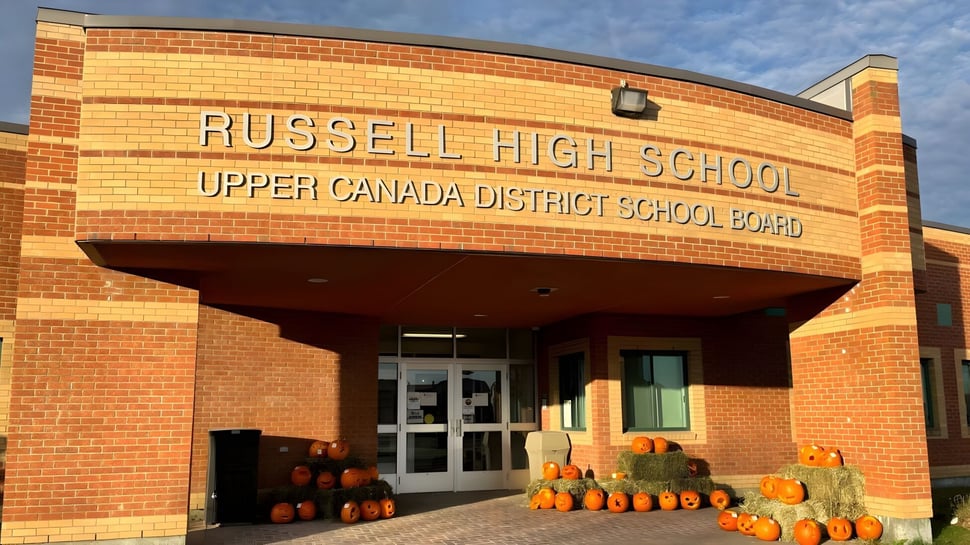 La entrada de Russell High School con un cartel del Upper Canada District School Board y una decoración de calabaza en primer plano.