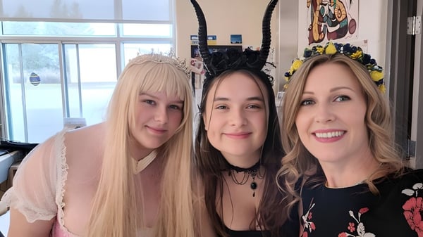 Tres mujeres sonriendo con diferente color de cabello posan frente a un colorido mural en Russell High School.