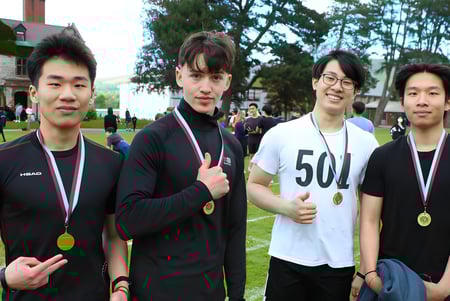 Cuatro estudiantes de la Ruthin School están en un campo de césped con medallas después de una competencia deportiva.