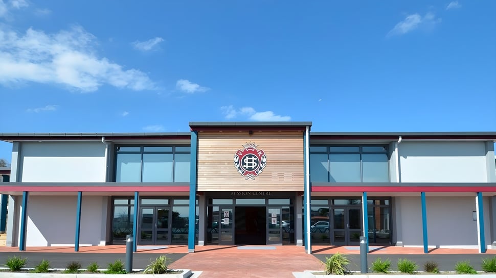 El moderno edificio de varios pisos con un gran emblema en la fachada del Sacred Heart College Napier bajo un cielo azul.