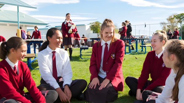 Alumnas y alumnos del Sacred Heart College Napier sentados al aire libre sobre la hierba frente a un edificio escolar.
