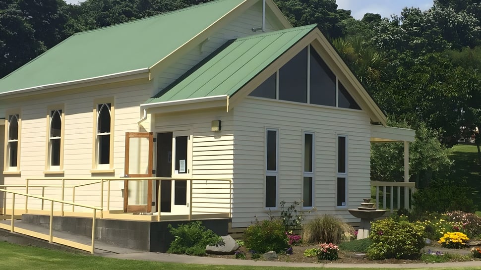 Una encantadora casa de madera con techo de metal verde se encuentra en medio de árboles y un jardín bien cuidado en el terreno del Sacred Heart Girls' College en New Plymouth.