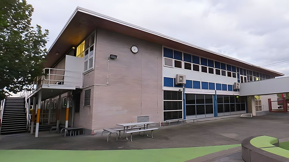 El moderno edificio de varios pisos del Sacred Heart Girls' College en Hamilton con grandes ventanas y un área de descanso cubierta al aire libre.