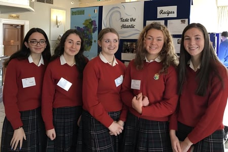 Cinco alumnas de la Sacred Heart Secondary School Clonakilty están juntas en el pasillo de la escuela frente a coloridos carteles.