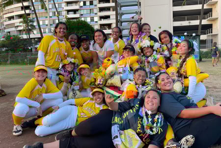 Un grupo de estudiantes de la Sacred Hearts Academy se reúne afuera frente a edificios con palmeras de fondo.