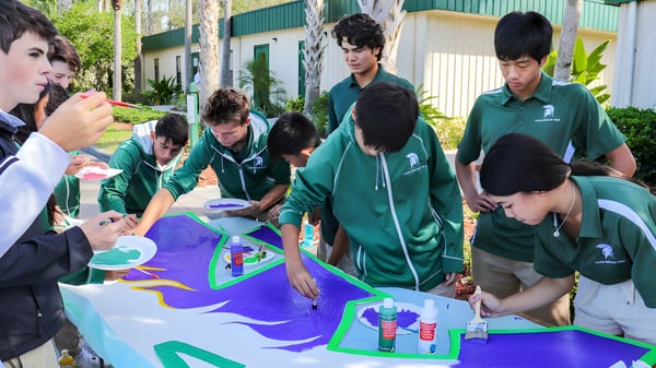 Estudiantes de la Saddlebrook Preparatory School trabajan juntos en un gran y colorido proyecto artístico sobre una mesa.