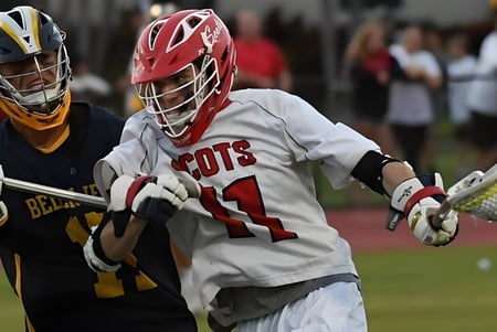 Dos jugadores de lacrosse de la Saint Andrews School luchan en el campo deportivo en un partido entre ellos.