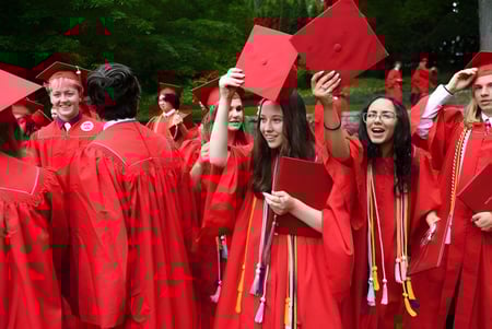 Los graduados de la Saint Bernard School celebran al aire libre con togas rojas y sostienen sus diplomas en alto.