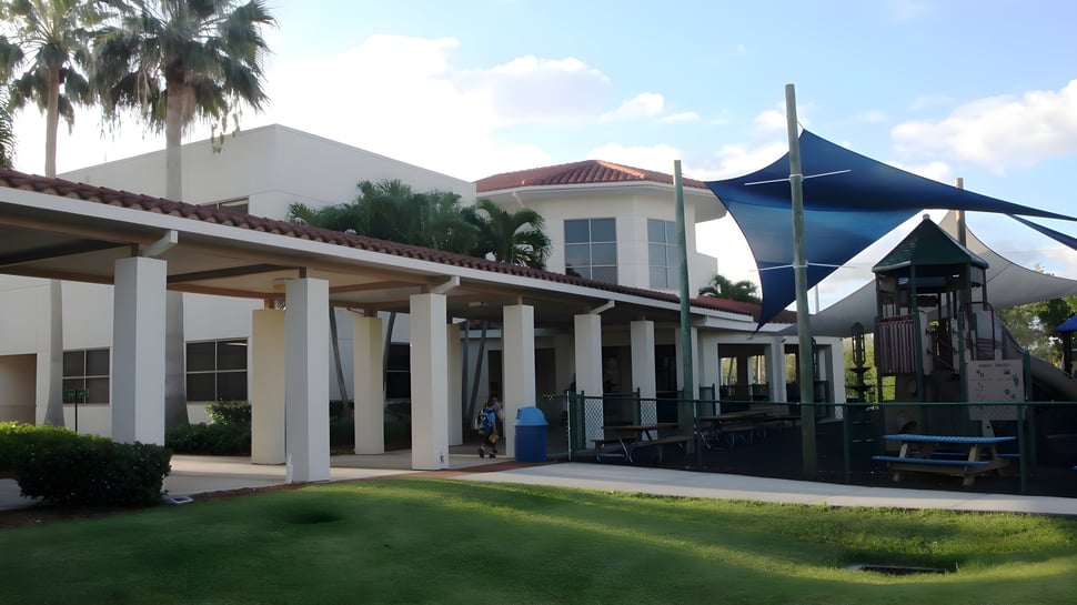 El moderno edificio de varios pisos de la Saint Edward's School está rodeado de palmeras y una superficie de césped con una sombrilla azul.